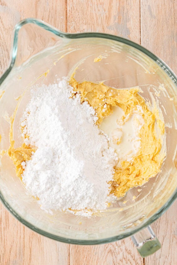 Heavy cream and powdered sugar being added to butter in a mixing bowl.