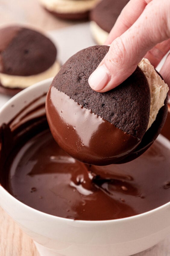 A whoopie pie being dipped into melted chocolate.