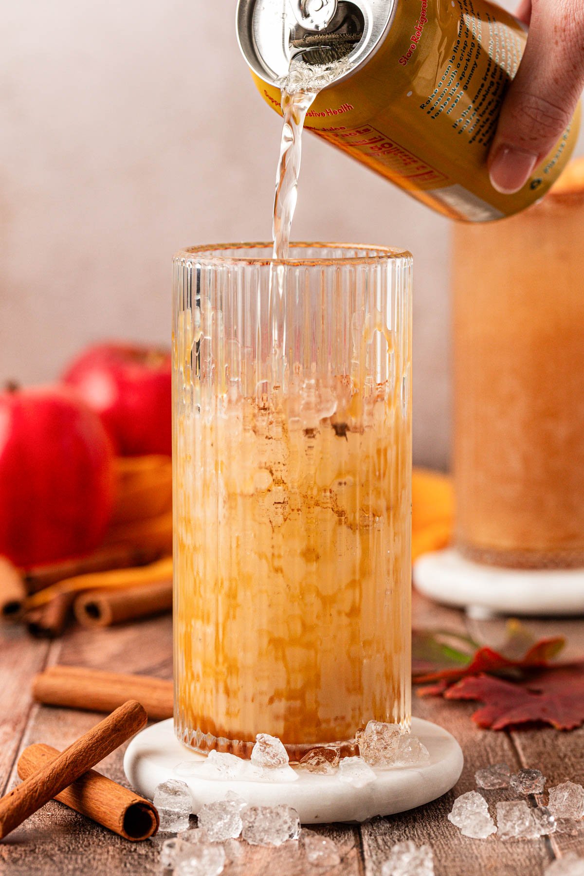 A can of apple olipop being poured into a glass with ice and caramel.