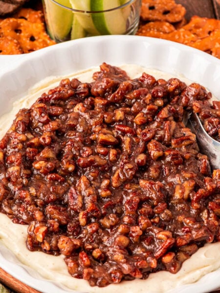 Pecan pie dip in a white dish surrounded but fruit and pretzels.
