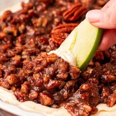 Close up of an apple slice dipping into a bowl of pecan pie dip.