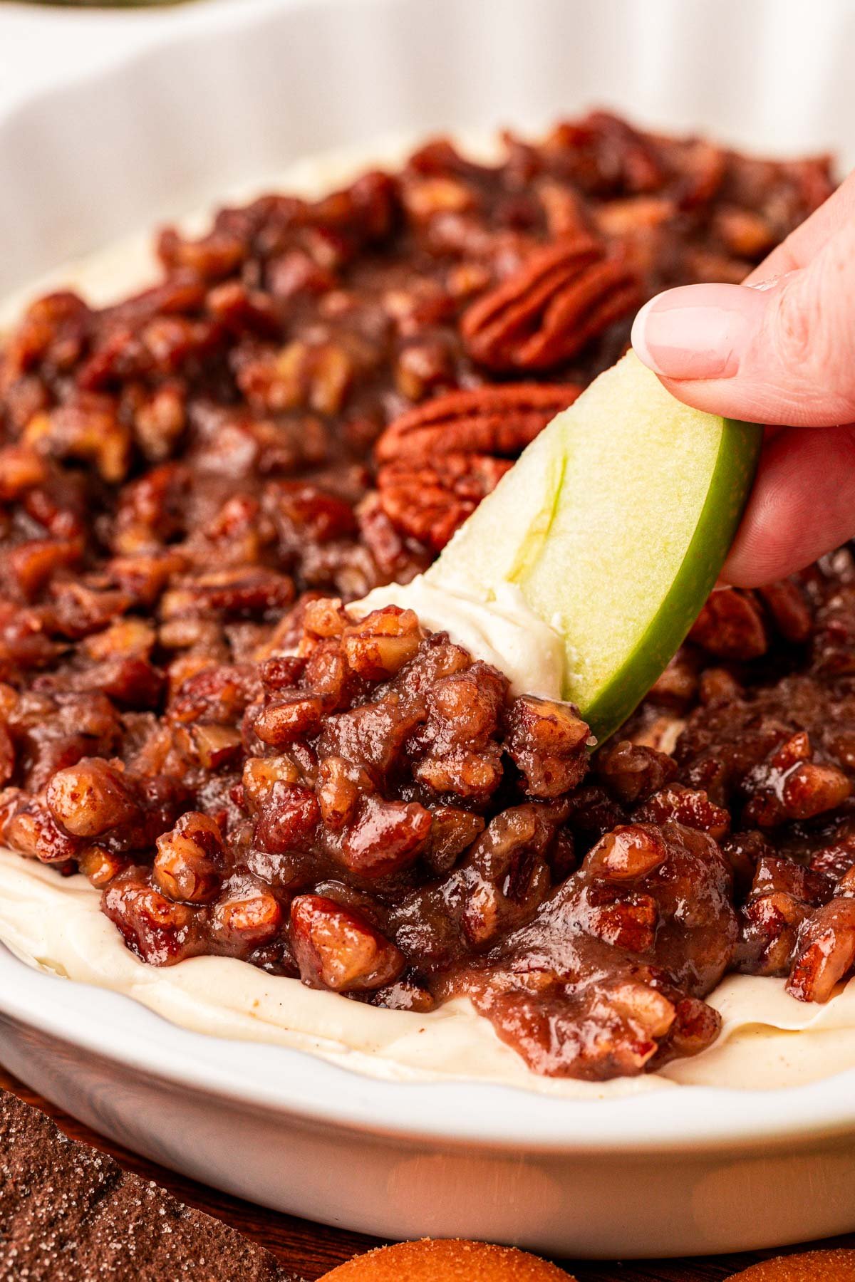 Close up of an apple slice dipping into a bowl of pecan pie dip.