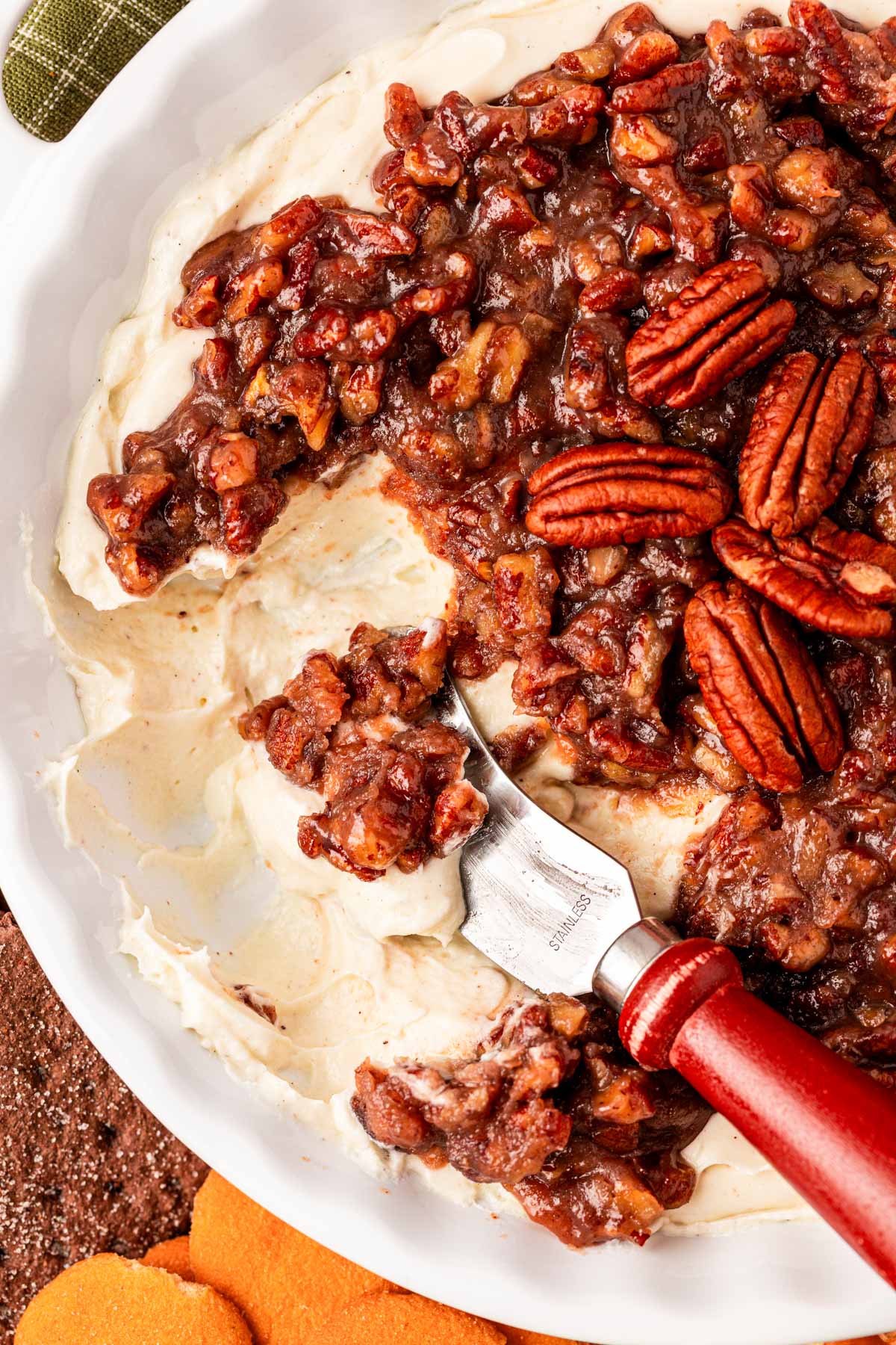 Pecan pie dip with a cheesecake layer in a white dish with a serving knife in it.
