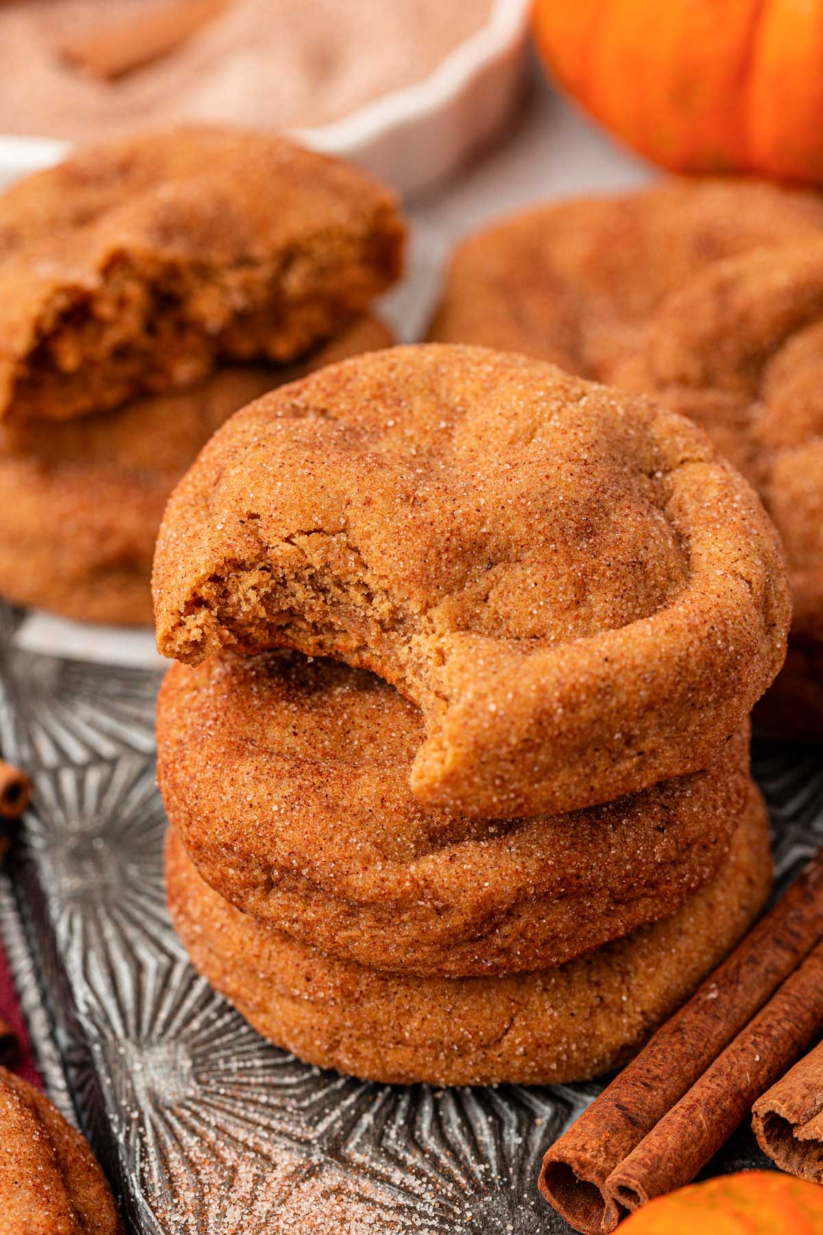 Close up of a sheet pan with pumpkin snickerdoodle cookies on it, the top cookie on the stack is missing a bite.