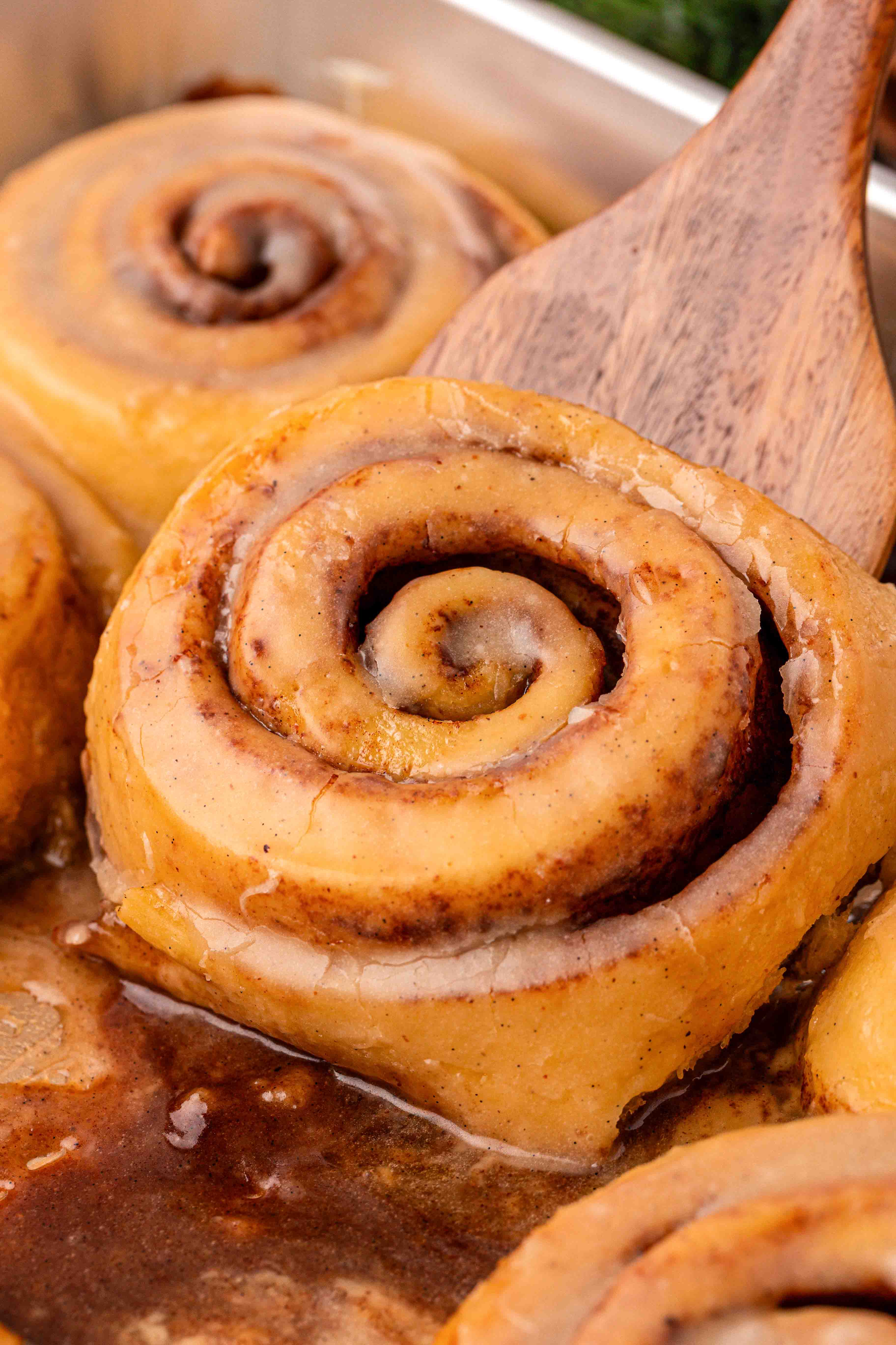 Eggnog cinnamon rolls in a pan with a spatula scooping one out.