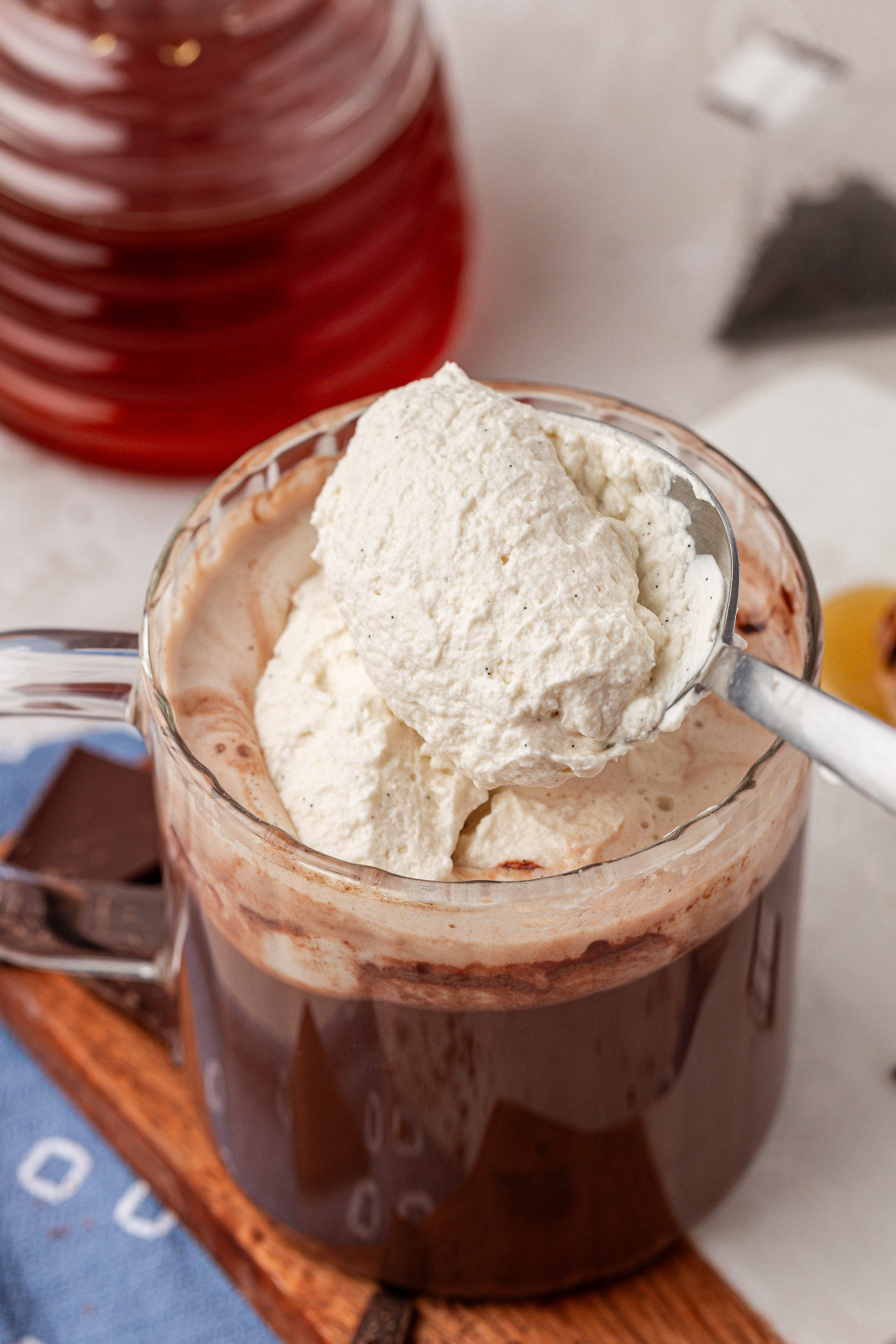 A spoon scooping whipped cream onto a mug of hot chocolate.