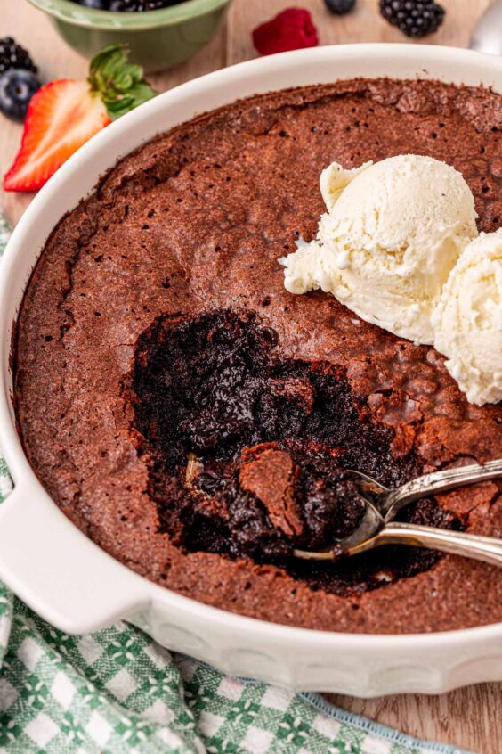 Brownie Pudding with spoons in it and vanilla ice cream scoops on top.