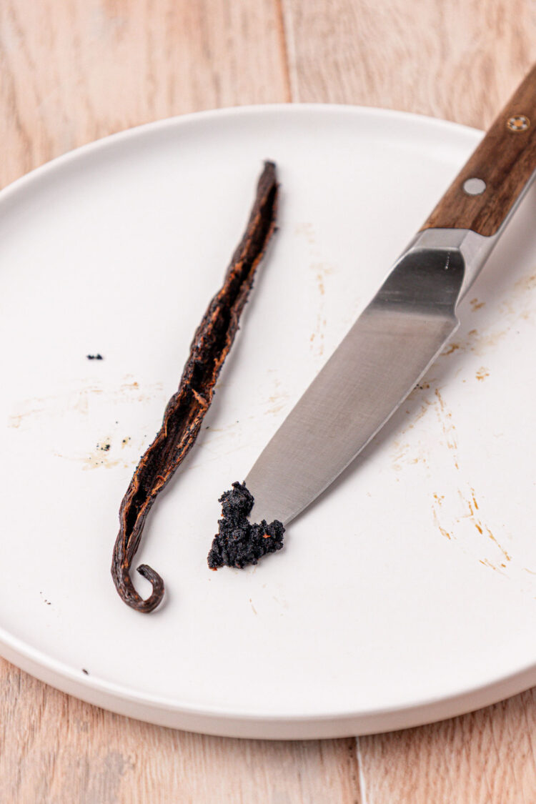 A paring knife with vanilla bean caviar on it on a white plate.