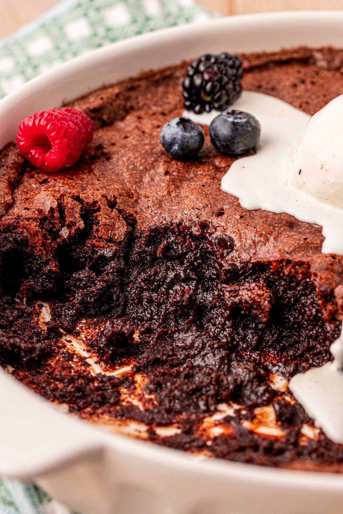 Close up of brownie pudding that's been partially served and topped with ice cream and berries.