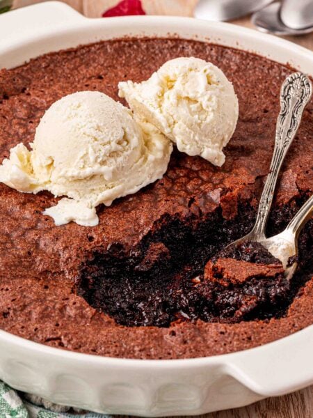 A dish of brownie pudding with two spoons in it a two scoops of vanilla ice cream on top.
