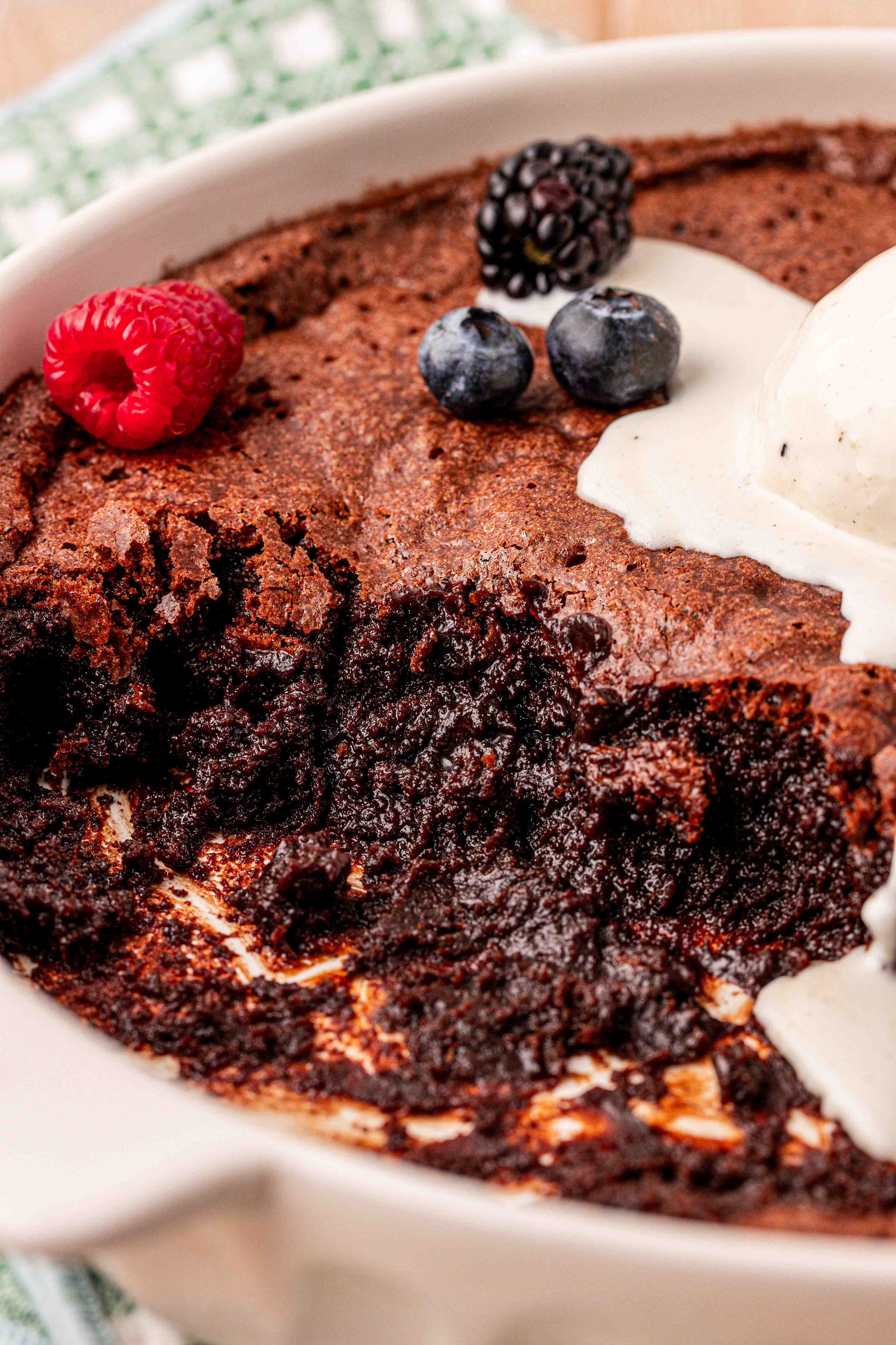 Close up of brownie pudding that's been partially served and topped with ice cream and berries.