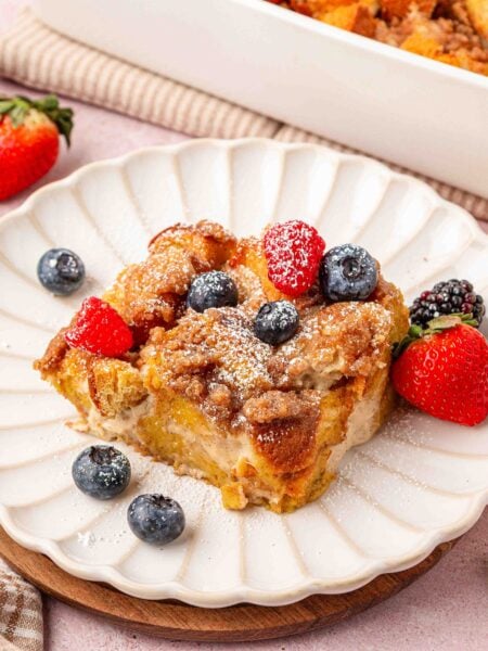 A slice of french toast casserole on a white scalloped plate with fresh berries on it.