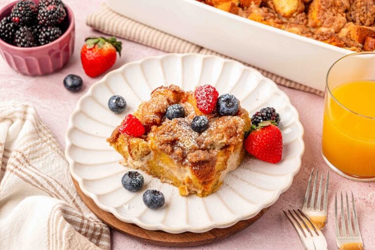 A slice of french toast casserole on a white scalloped plate with fresh berries on it.