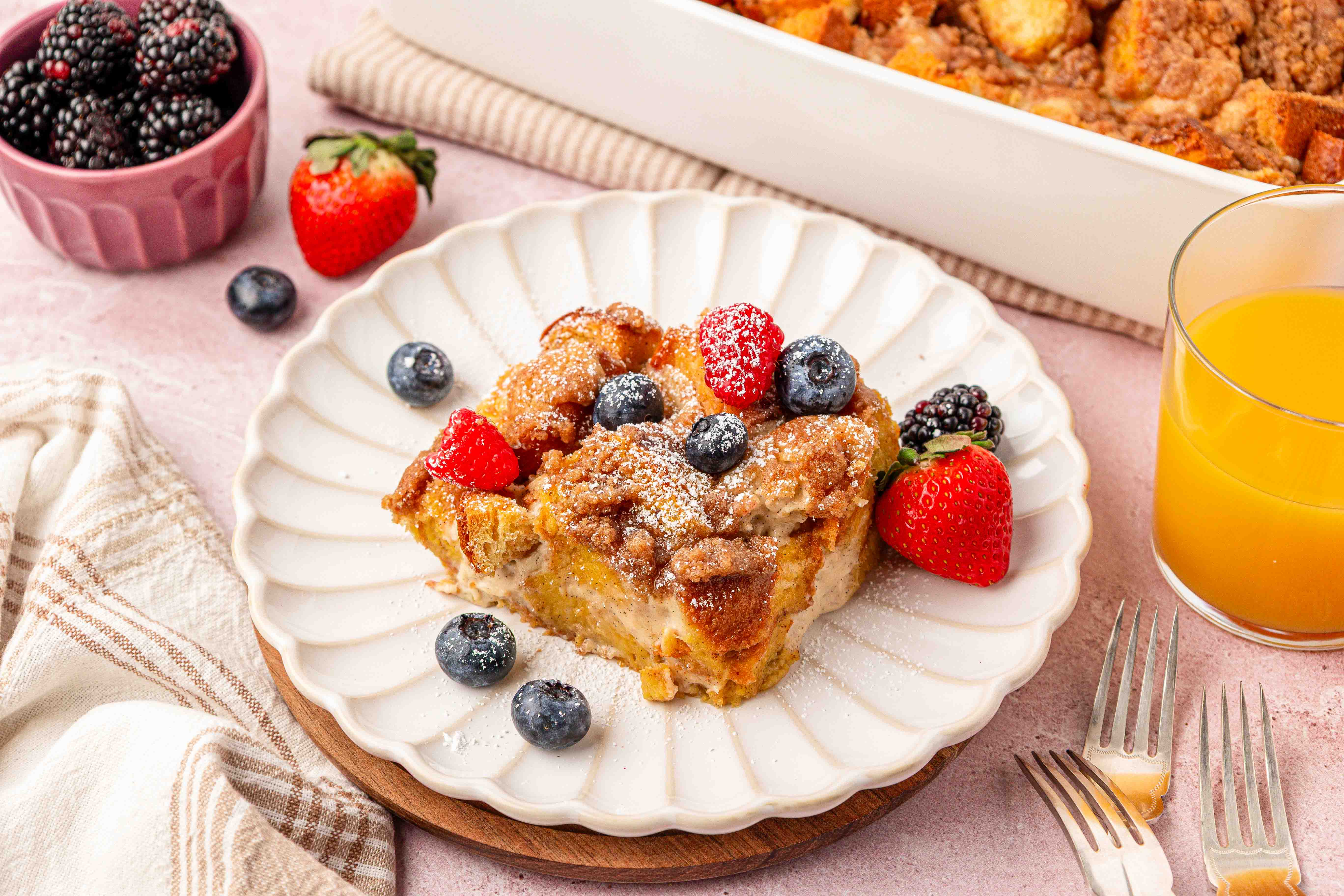 A slice of french toast casserole on a white scalloped plate with fresh berries on it.