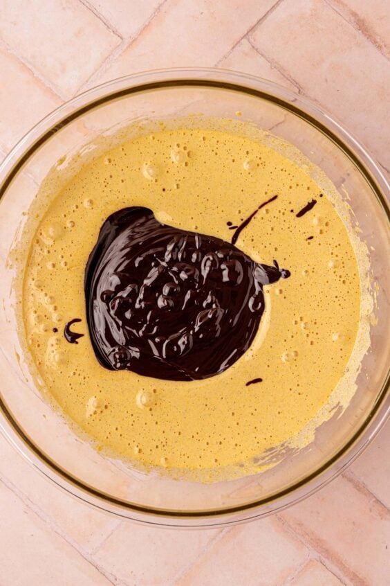 Melted chocolate mixture being added to whipped egg yolks and sugar.