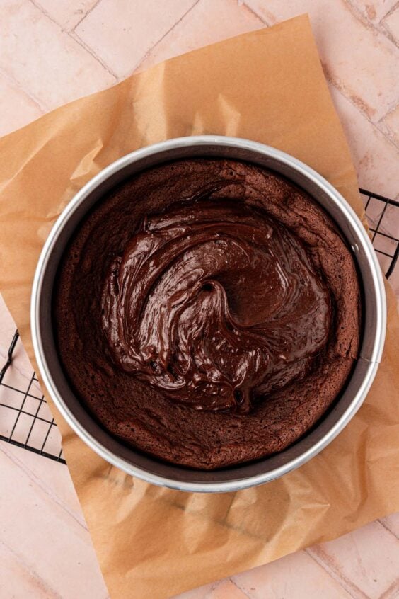 Chocolate cake batter being added to the top of a baked chocolate cake.