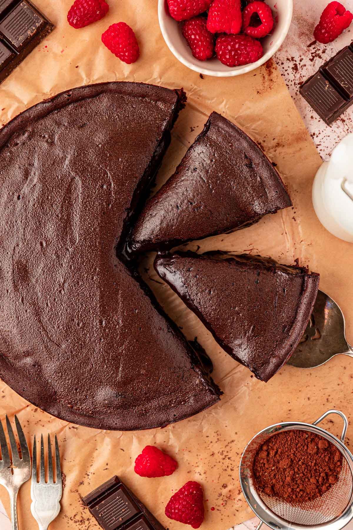 Overhead photo of French Moelleux au Chocolat Cake on a piece of parchment paper with some slices next to it.