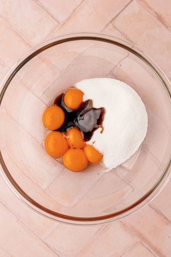 Egg yolks, sugar, and vanilla bean paste in a glass bowl.