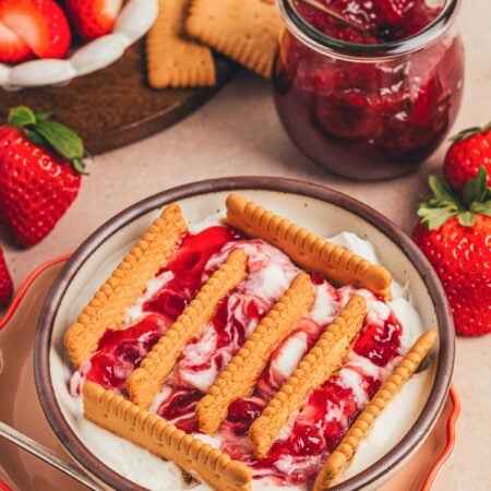 A bowl of Japanese cheesecake with strawberry jam and biscuits sticking out.