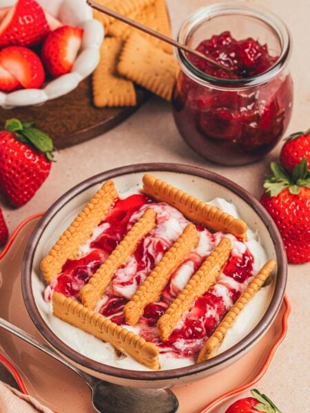 A bowl of Japanese cheesecake with strawberry jam and biscuits sticking out.