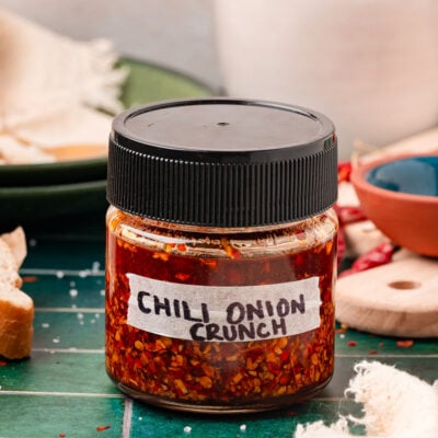 A jar of homemade chili onion crunch with a black top on a green table.