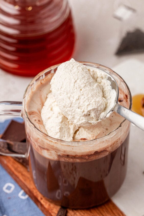 A spoon scooping whipped cream onto a mug of hot chocolate.
