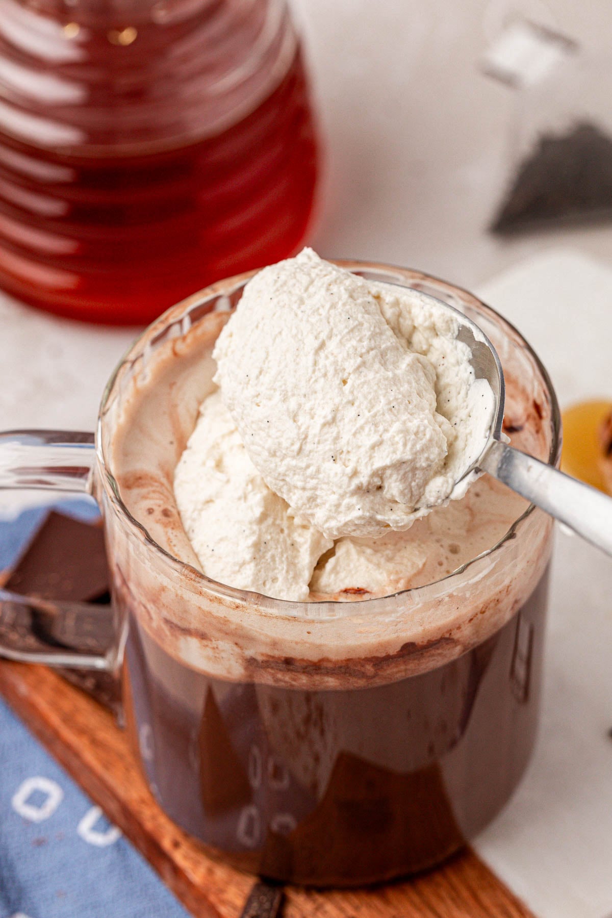 A spoon scooping whipped cream onto a mug of hot chocolate.