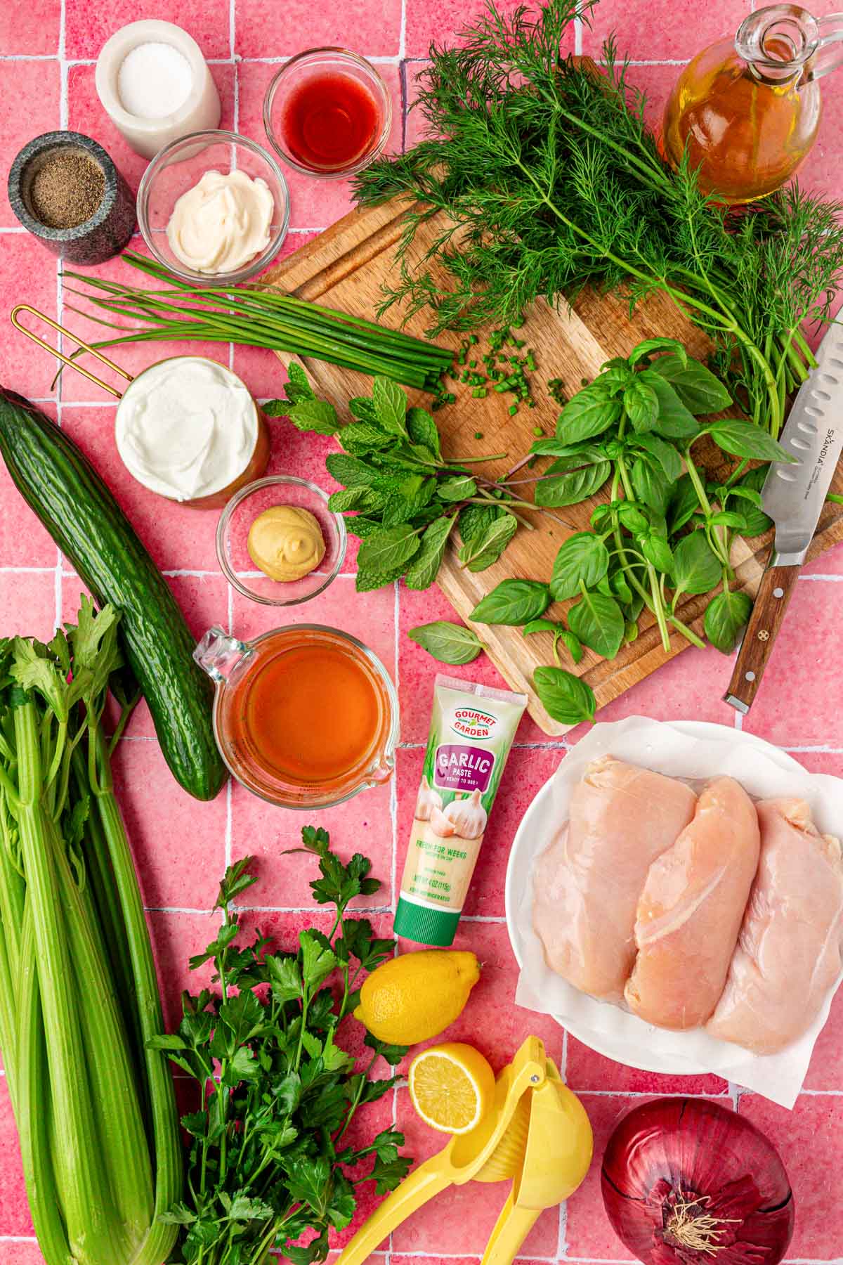 Ingredients to make chicken salad with green goddess dressing on a pink table.