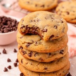 A stack of chocolate chip cookies. The top one is missing a bite.