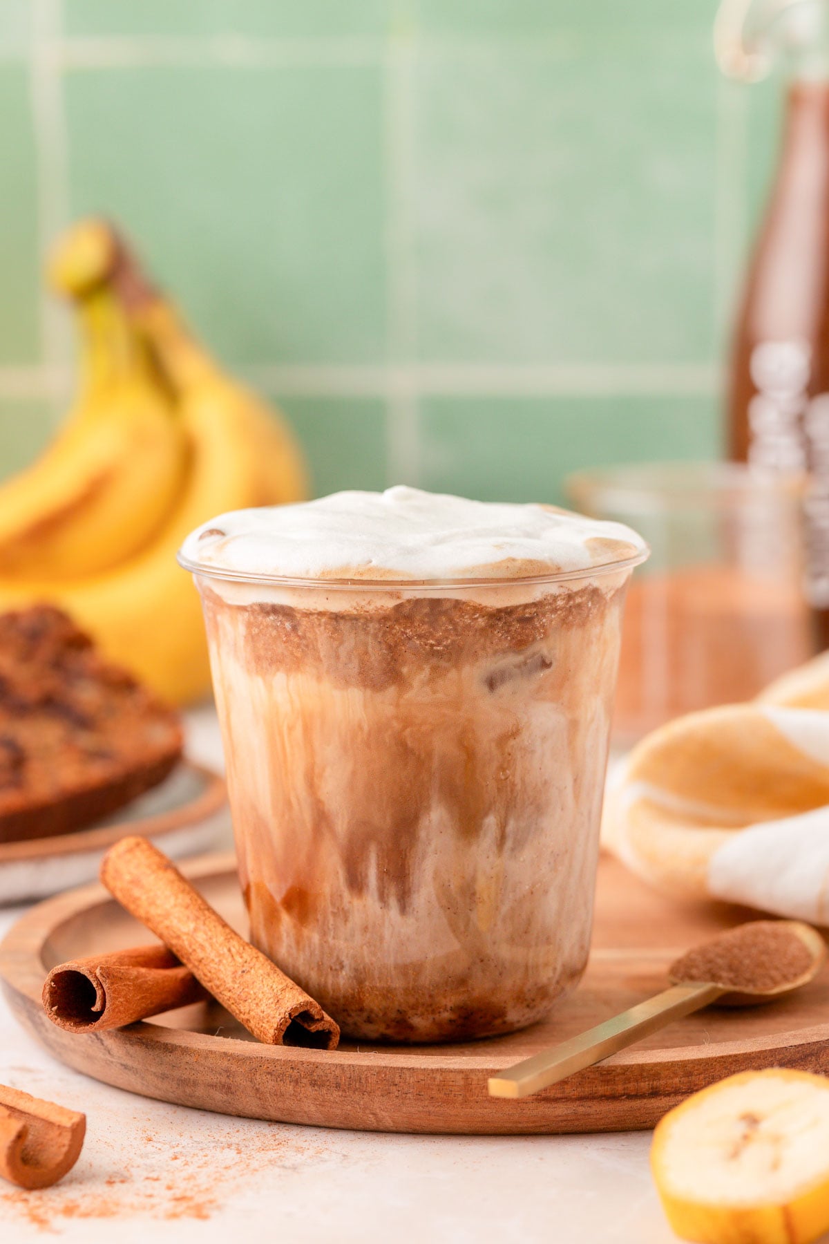 Banana bread latte on a wooden tray with bananas and cinnamon sticks in the background.