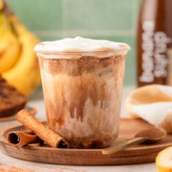 A cup with banana bread latte on a wooden tray.