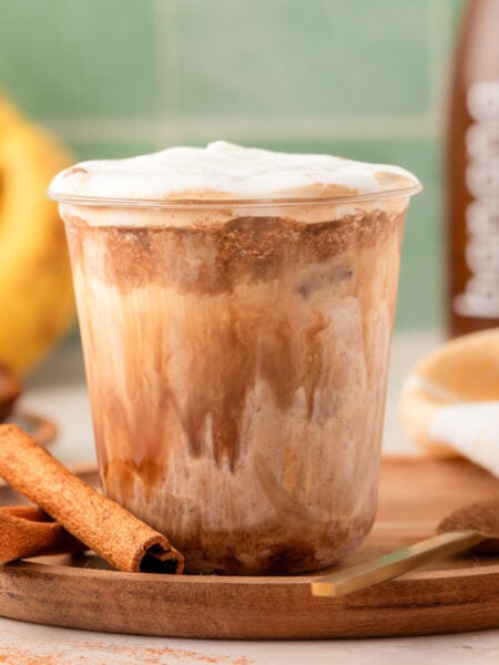 A cup with banana bread latte on a wooden tray.