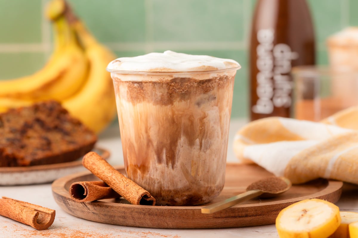 A cup with banana bread latte on a wooden tray.