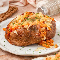 A large Jacket potato filled with shredded cheese and baked beans on a white plate.