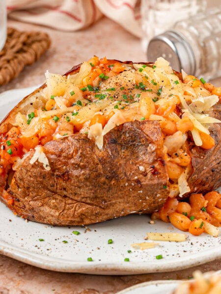 A large Jacket potato filled with shredded cheese and baked beans on a white plate.