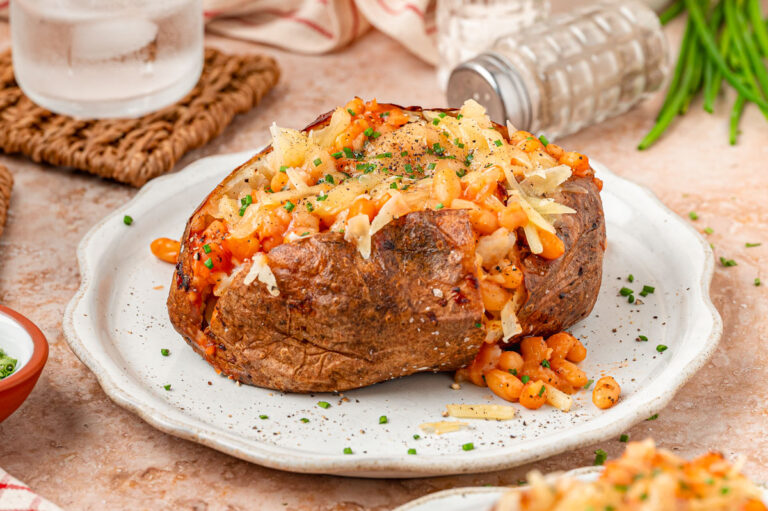 A large Jacket potato filled with shredded cheese and baked beans on a white plate.