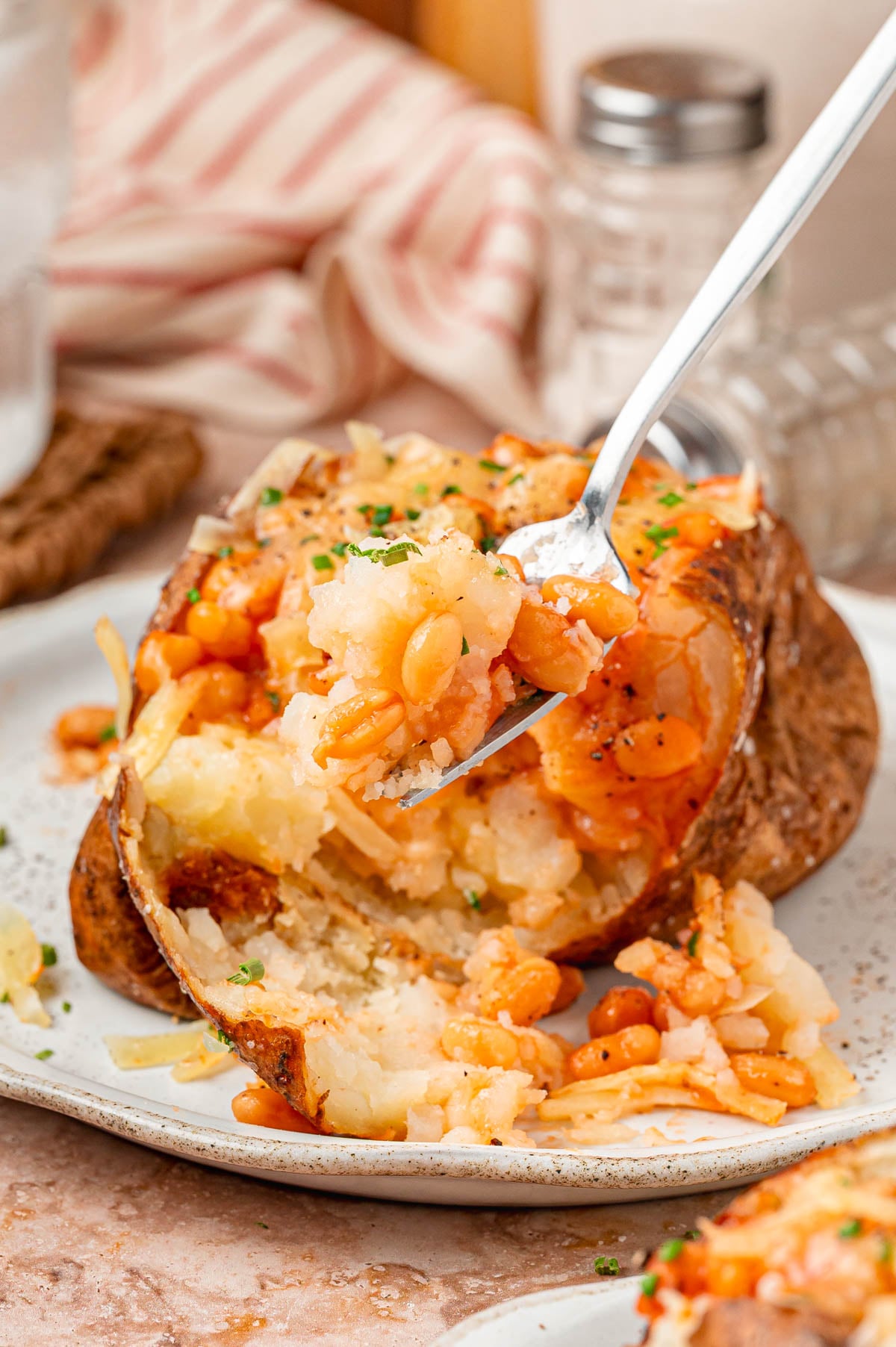 Close up of a fork full of a bite of jacket potato with cheese and baked beans.
