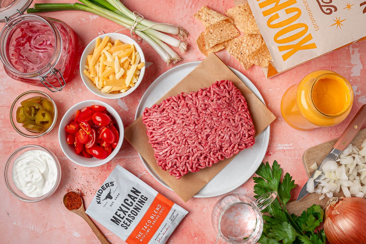 Ingredients to make sheet pan nachos on a pink table.