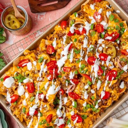 Overhead photo of sliding nachos on a sheet pan garnished with sour cream and tomatoes and peppers.