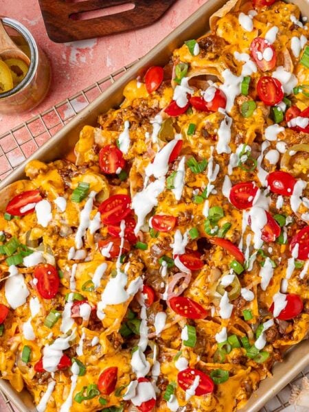 Overhead photo of sliding nachos on a sheet pan garnished with sour cream and tomatoes and peppers.