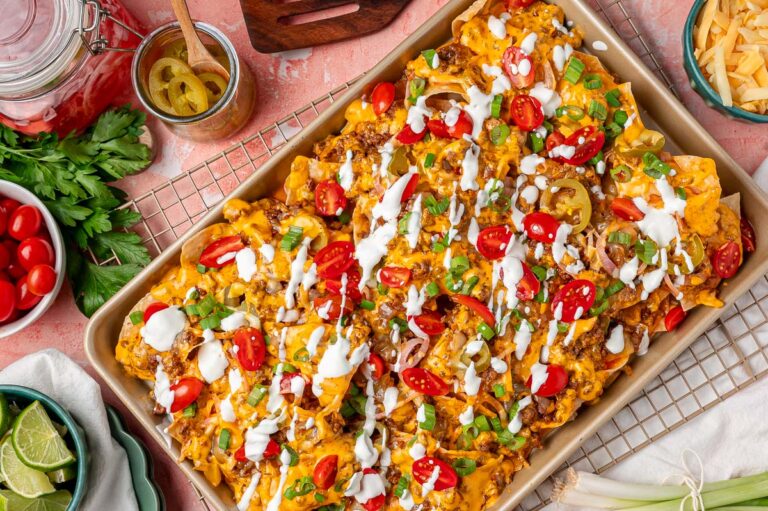 Overhead photo of sliding nachos on a sheet pan garnished with sour cream and tomatoes and peppers.