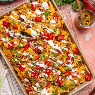 Overhead photo of a sheet pan with nachos on it on a pink table.