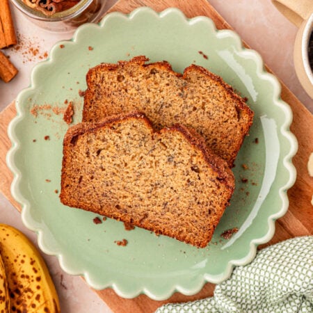 Two slices of banana bread on a scalloped green plate on a table.