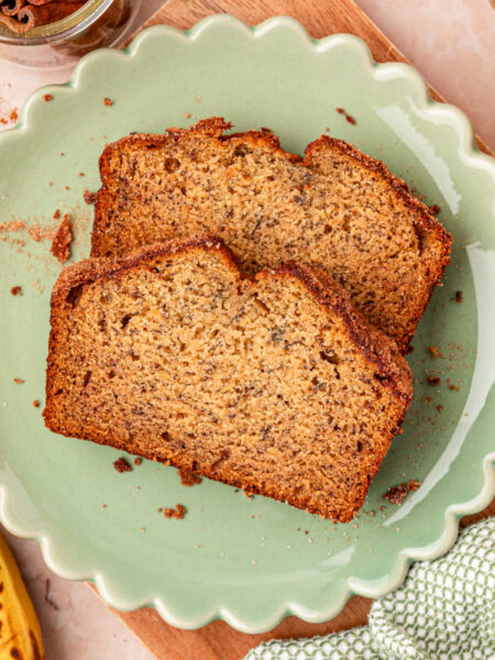 Two slices of banana bread on a scalloped green plate on a table.