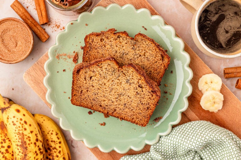 Two slices of banana bread on a scalloped green plate on a table.
