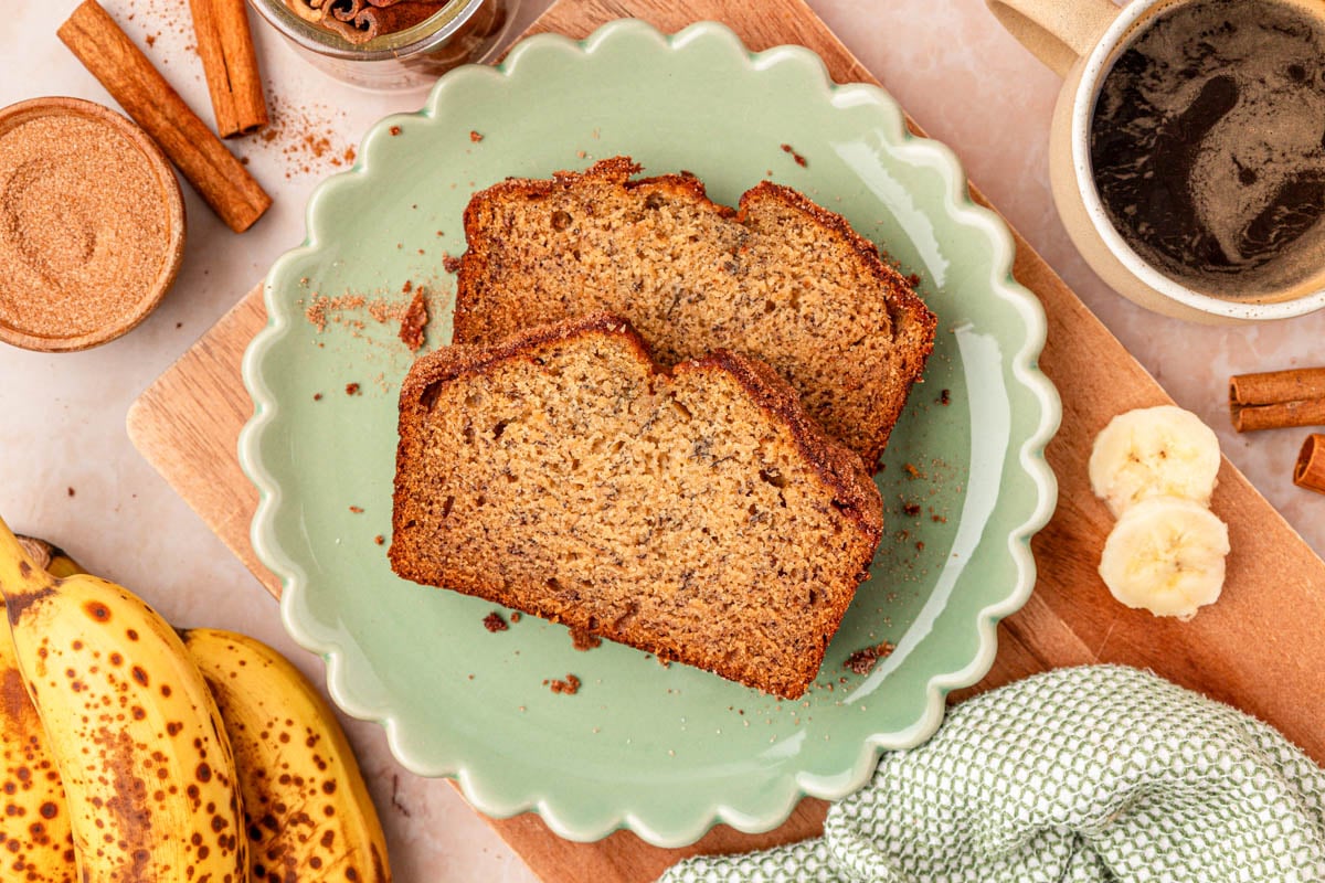 Two slices of banana bread on a scalloped green plate on a table.