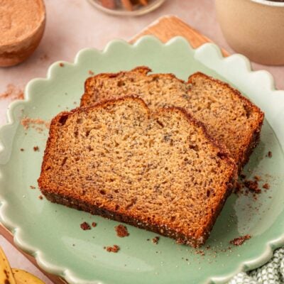 Two slices of banana bread on a scalloped green plate on a table.