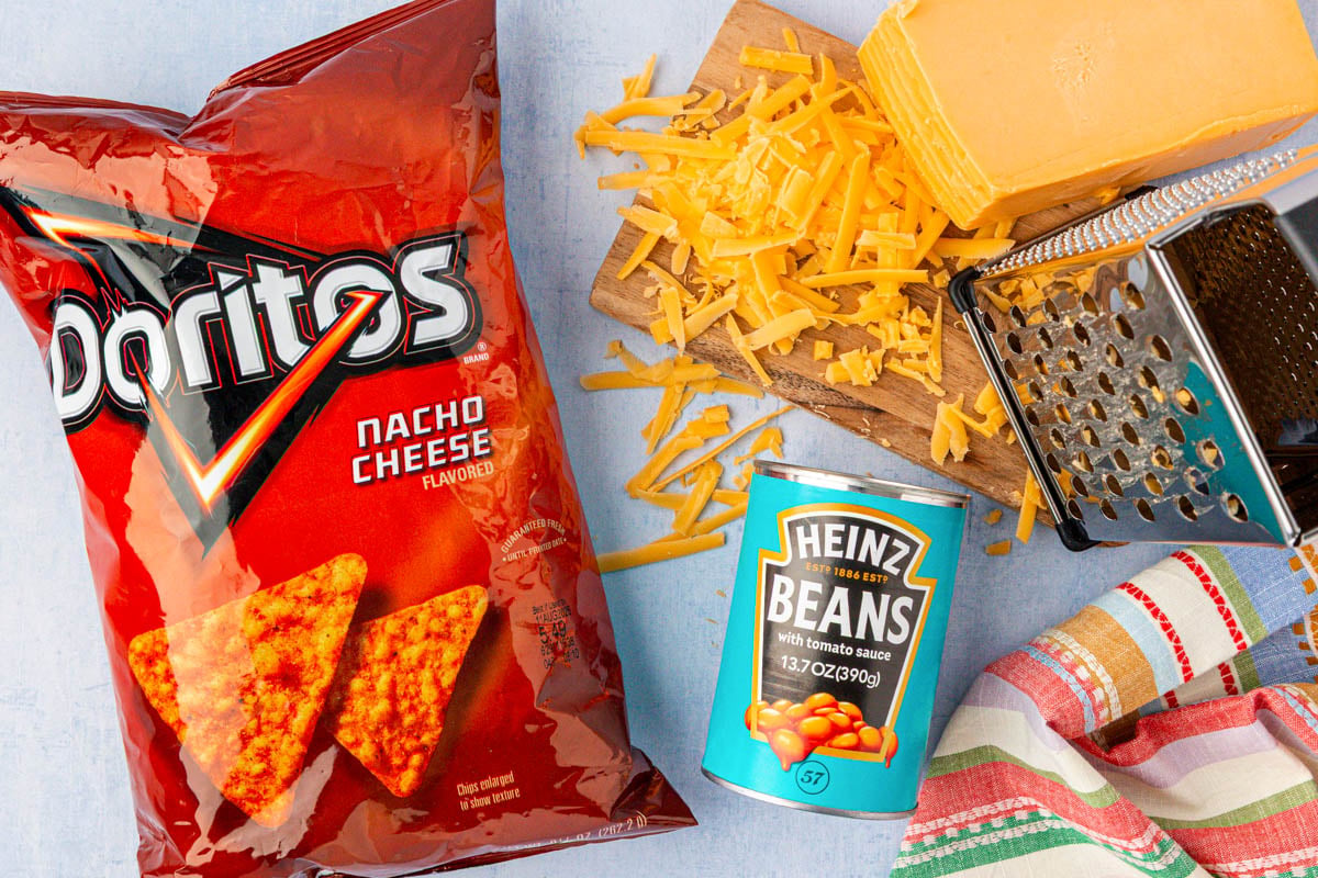 A bag of Doritos, a can of baked beans, and a block of cheese on a table.