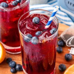 Two glasses of red-toned iced tea with blueberries on a serving board.