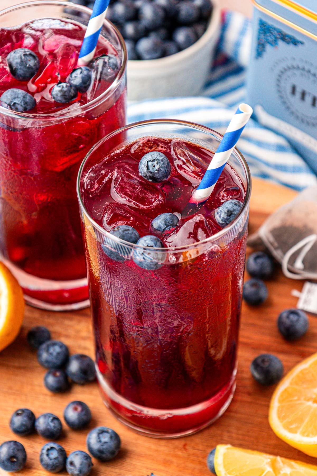 Two glasses of red-toned iced tea with blueberries on a serving board.